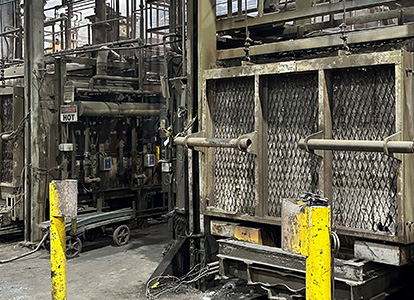 The image shows an industrial interior with heavy machinery, metallic structures, dirty floors, pipes, and possibly a production assembly area or factory setting.