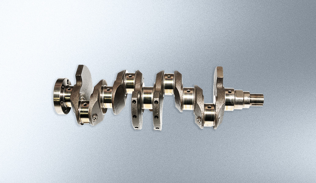 This is an image of a metal crankshaft on a grey background. It's a key component in an internal combustion engine, essential for converting linear motion to rotation.