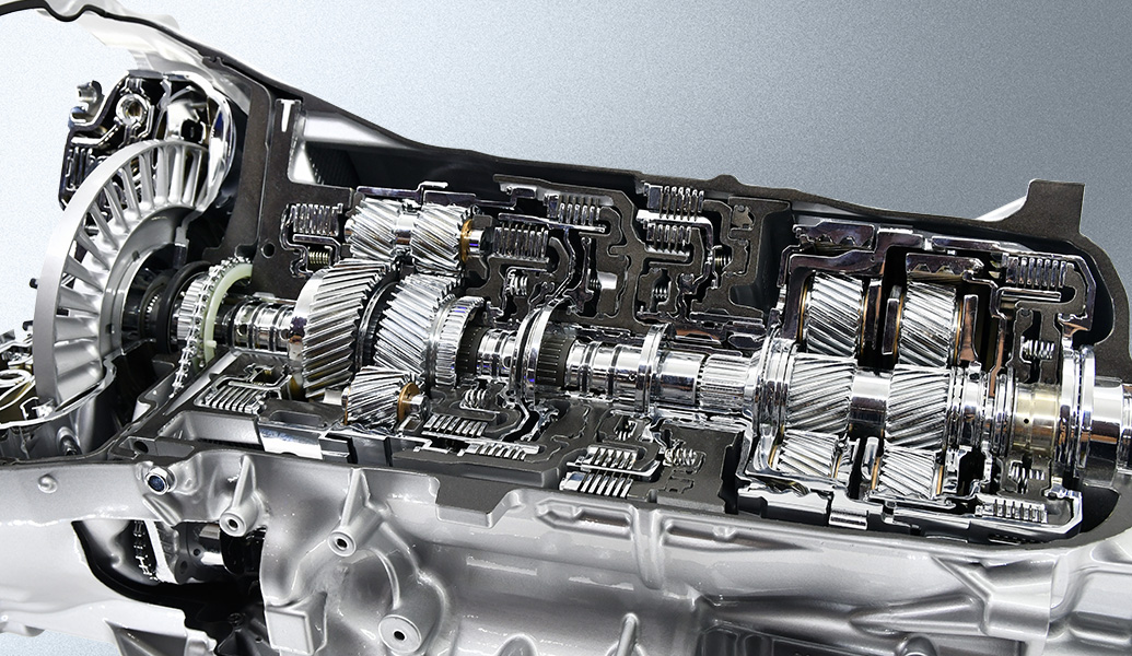 This image displays a cross-section of a modern automatic transmission system, showcasing gears, shafts, and hydraulic paths in a metallic casing.