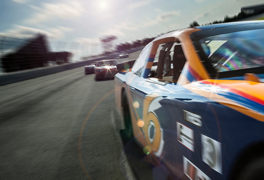 A dynamic race track scene with a close-up of a racing car in motion, likely during a competitive event, with blurred background suggesting high speed.