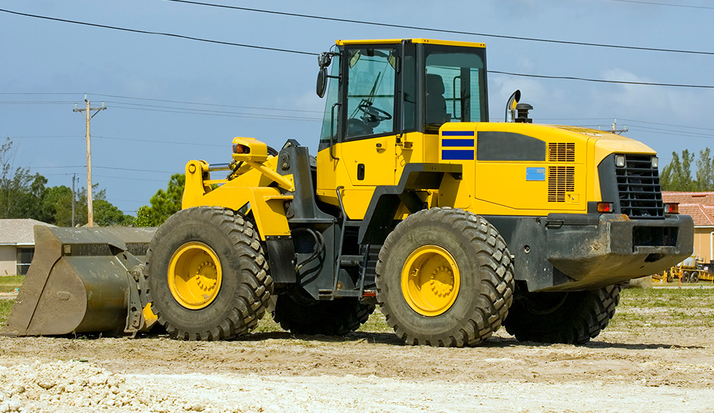 A yellow and black wheel loader with a front bucket parked on a gravel surface, under a clear sky, likely at a construction or industrial site.