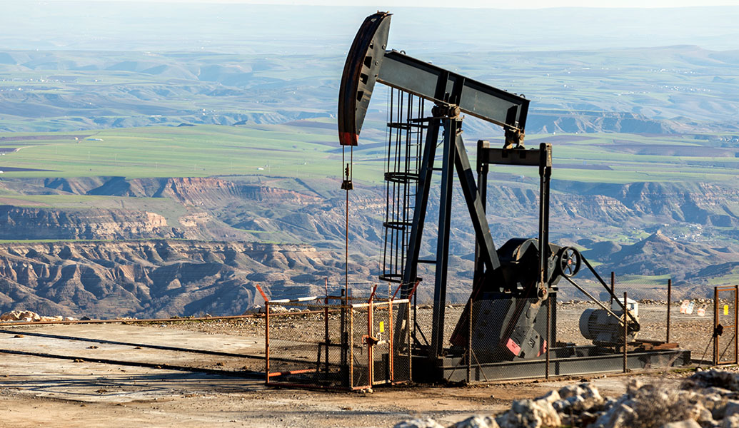 This is an oil pump jack located on arid land, with vast open fields and canyons in the background under a clear sky.