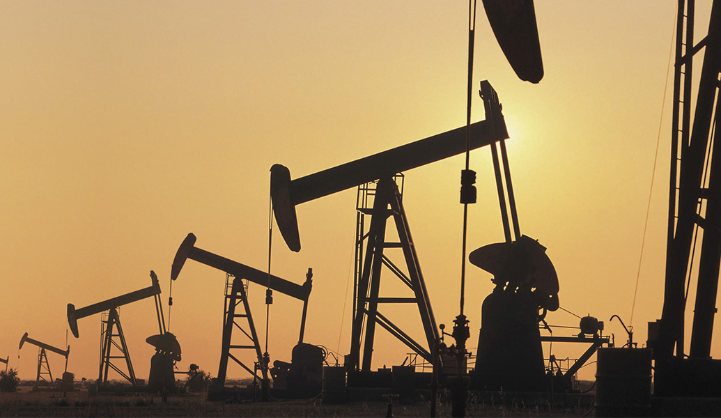 This image depicts multiple oil pumpjacks silhouetted against a glowing sunset sky, illustrating an industrial landscape dedicated to energy extraction.