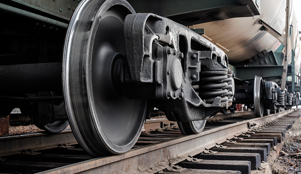 Close-up of a train's wheelset on tracks, showcasing the wheels, axles, and suspension components with a focus on engineering and mechanical design.