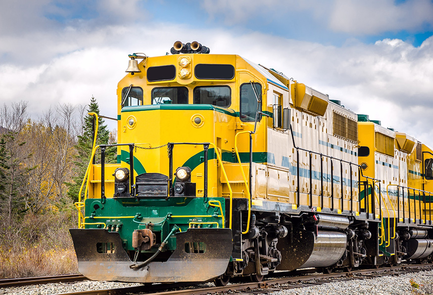 A vibrant yellow and white locomotive is positioned on train tracks under a cloudy sky, showcasing its bold colors and robust design.