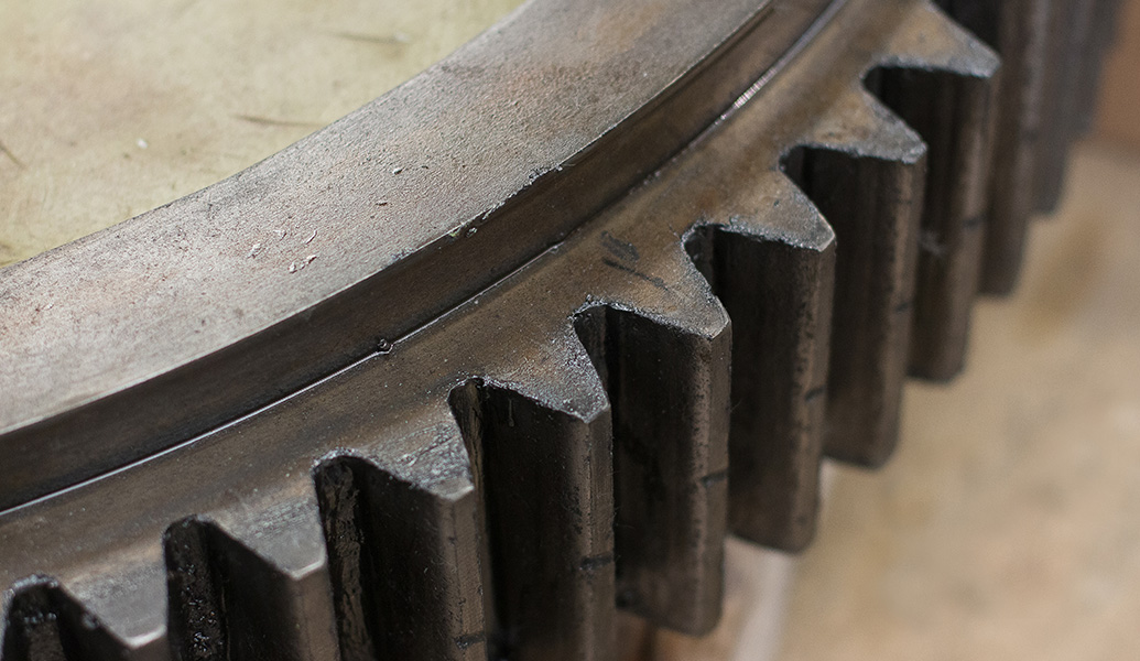 This image shows a close-up of a large gear with prominent, interlocking teeth, possibly from industrial machinery. The metal surfaces appear worn and used.