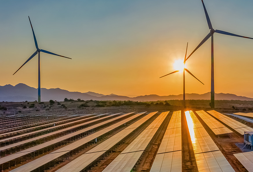 A renewable energy farm at sunset, featuring rows of solar panels and wind turbines against a backdrop of distant mountains and a colorful sky.