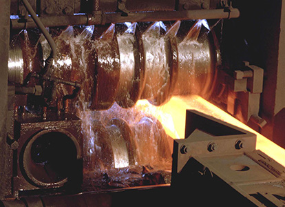 The image shows a close-up of industrial machinery, specifically a molten metal casting process, with fiery liquid metal being poured into a mold.