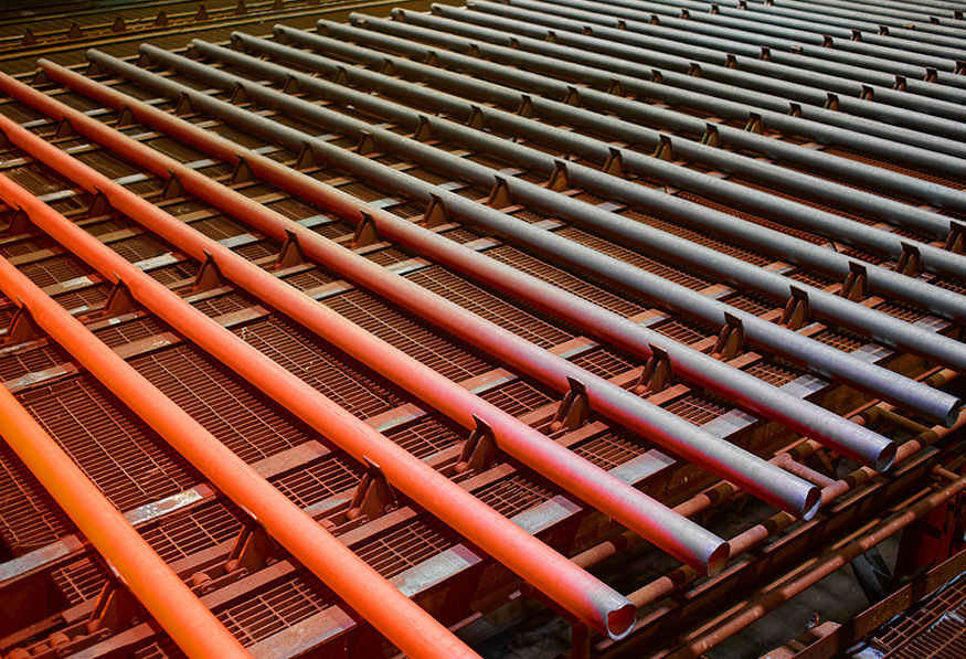 The image shows a repetitive pattern of large bulky red pipes arranged neatly over a grating surface, possibly part of an industrial or manufacturing setting.