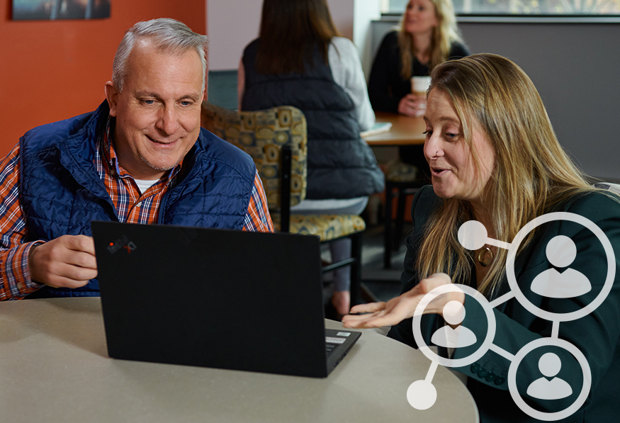 Two people are looking at a laptop screen with interest, possibly working together. Graphic icons suggesting a social network overlay the image. They're indoors.