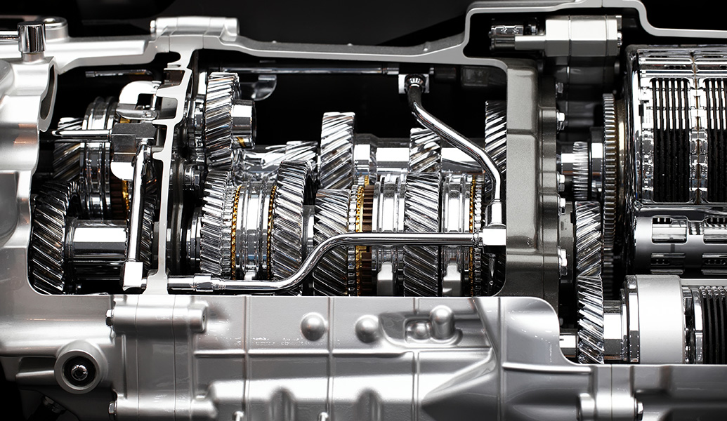 A close-up of a complex vehicle gearbox section, revealing intricate gears and cogs within a metallic casing against a dark background.